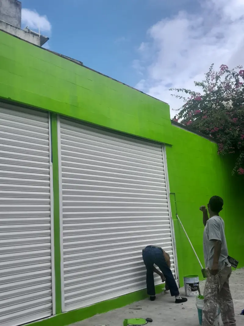 Pintores aplicando pintura verde en la fachada de un local comercial en Playa del Carmen